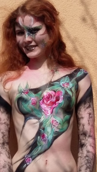 Bodypainting auf die Arme und über den vorderen Brustkorb einer Frau. In verschiedenen Farben sowie rot und grüntönen wurden Blumen gemalt. die Arme wurden in einem schwarzen Netzmuster geairbrusht.