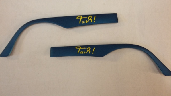 blaue Brillenbügel wurden angeschliffen und dann in einem gelbton den Schriftzug Tach aufgebrascht. Danach kam ein Klarlack darauf