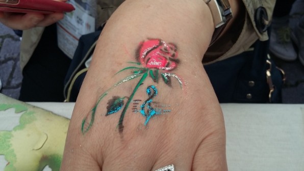 Bodypainting auf den Handrücken wird in rot,grün und blau Farben eine Rose geairbrusht