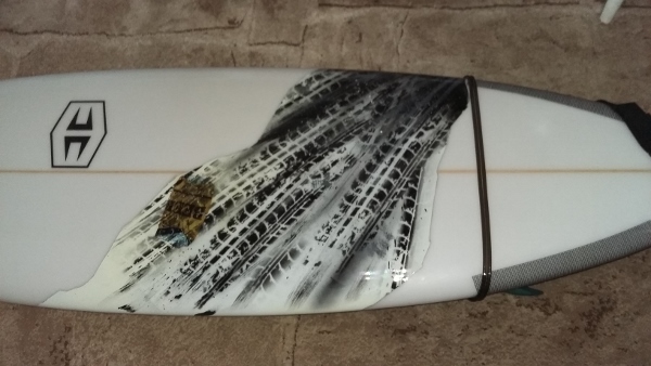 ein weißes Snowboard wurde grundiert und dann nochmal angeschliffen. es wurden mit einer selbstangefertigten Schablone Autoreifenspuren auf das Board geairbrusht. eine braunfarbene Bierdose wurde überfahren.