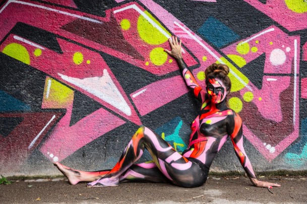 Airbrush-Bodypainting in einer Grafitiwand mit den Farben Pink, rosa blau und gelb Hintergrund ist schwarz