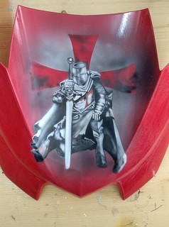 es wurde auf ein rotes Motorradteil ein ritter in schwarzweiss geairbrusht es ist ein Kreuz in rot und da schwert ist in weiss geairbrusht