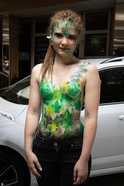 ein Event in einem Autohaus unter vielen neuen Autos. Bodypainting in grün für die Natur. Auf die Motorhaube ist ein marmor angebracht mit Blättern