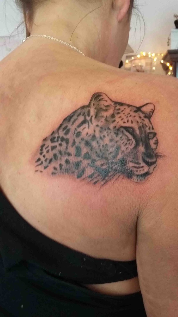 mit schwarzer Tattoofarbe wurde auf ein rechtes Schulterblatt einer Frau ein Leopard gestochen.