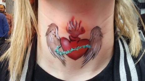 Es ist ein rotes Herz mit Flügel in grau und weißtönen auf dem Hals mittig. Das Herz hat einen grünen Stacheldrath drumherum